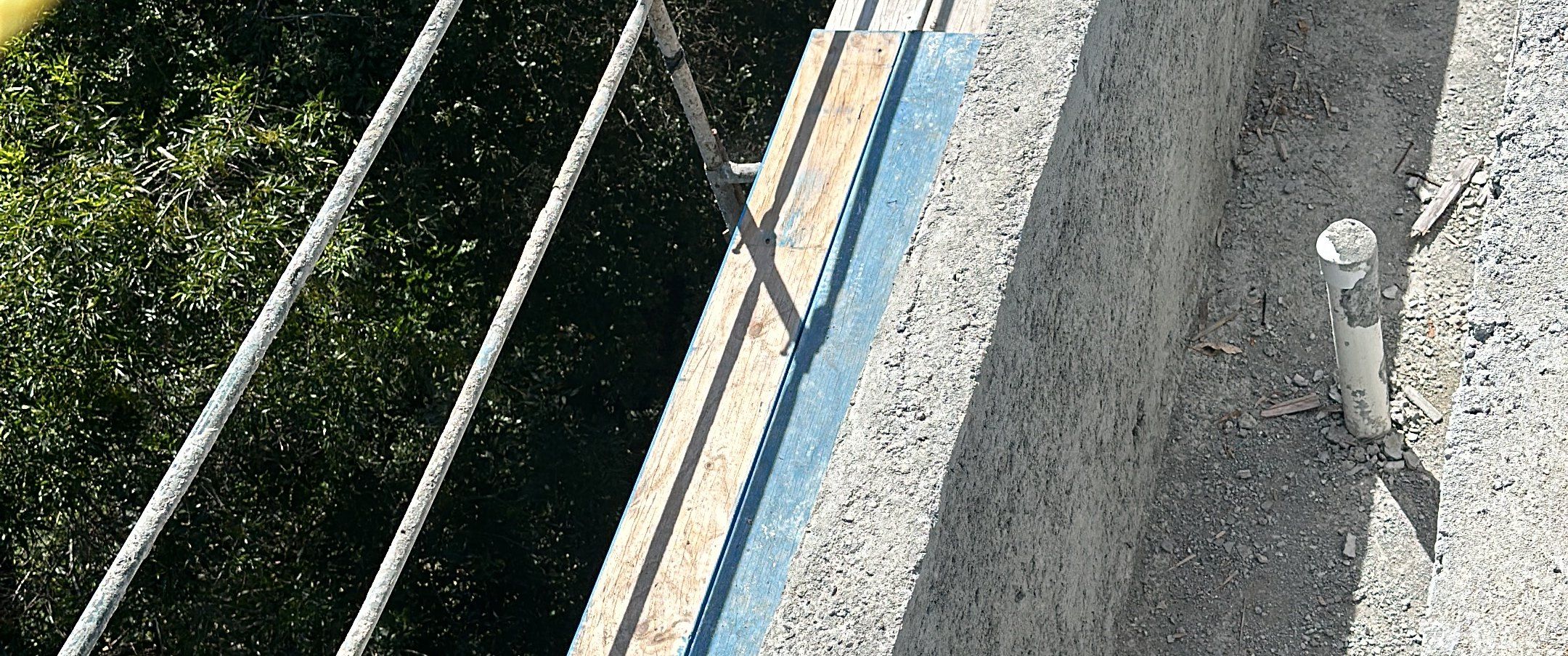 Looking down the top of a new poured concrete retaining wall on the steep Bel Air hillside lot, with trees below, an Akopi Builders build