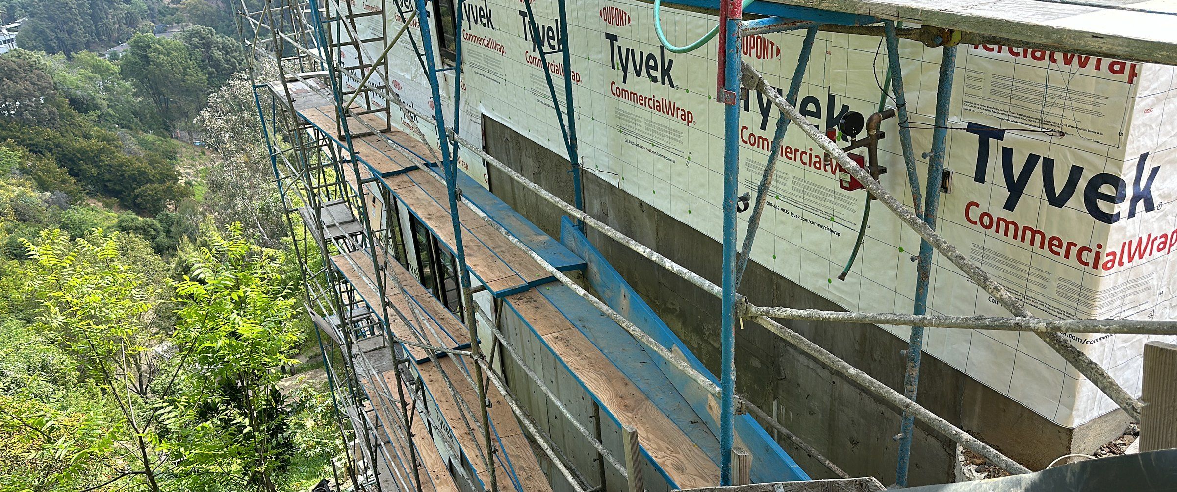 Scaffolding along the wrapped walls of the Akopi Builders custom home on a steep Bel Air canyon lot, with the hillside falling away below