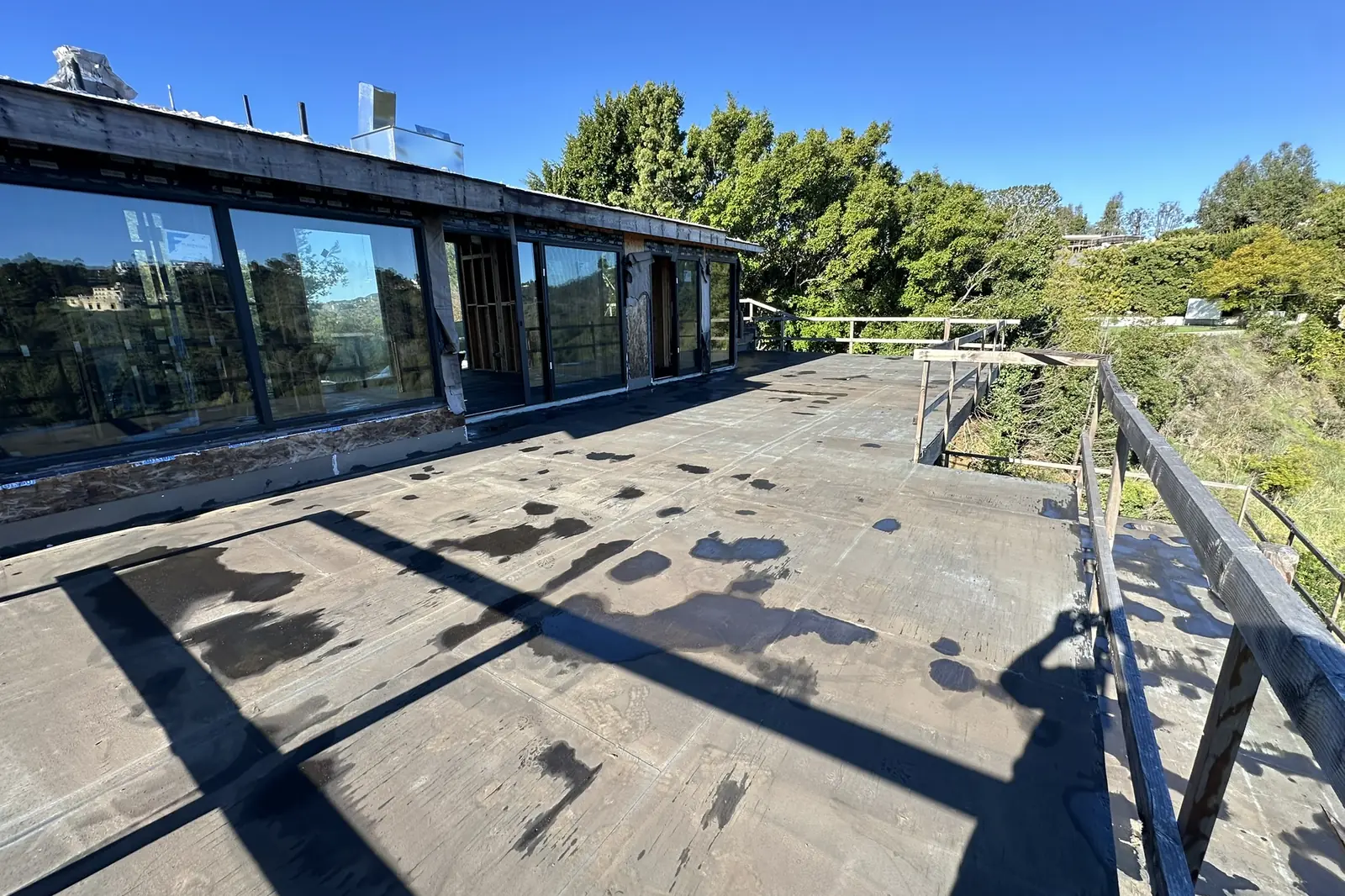 An upper deck with a steel railing on a hillside house under construction in Bel Air, with tall windows and the wooded canyon beyond, on an Akopi Builders project.