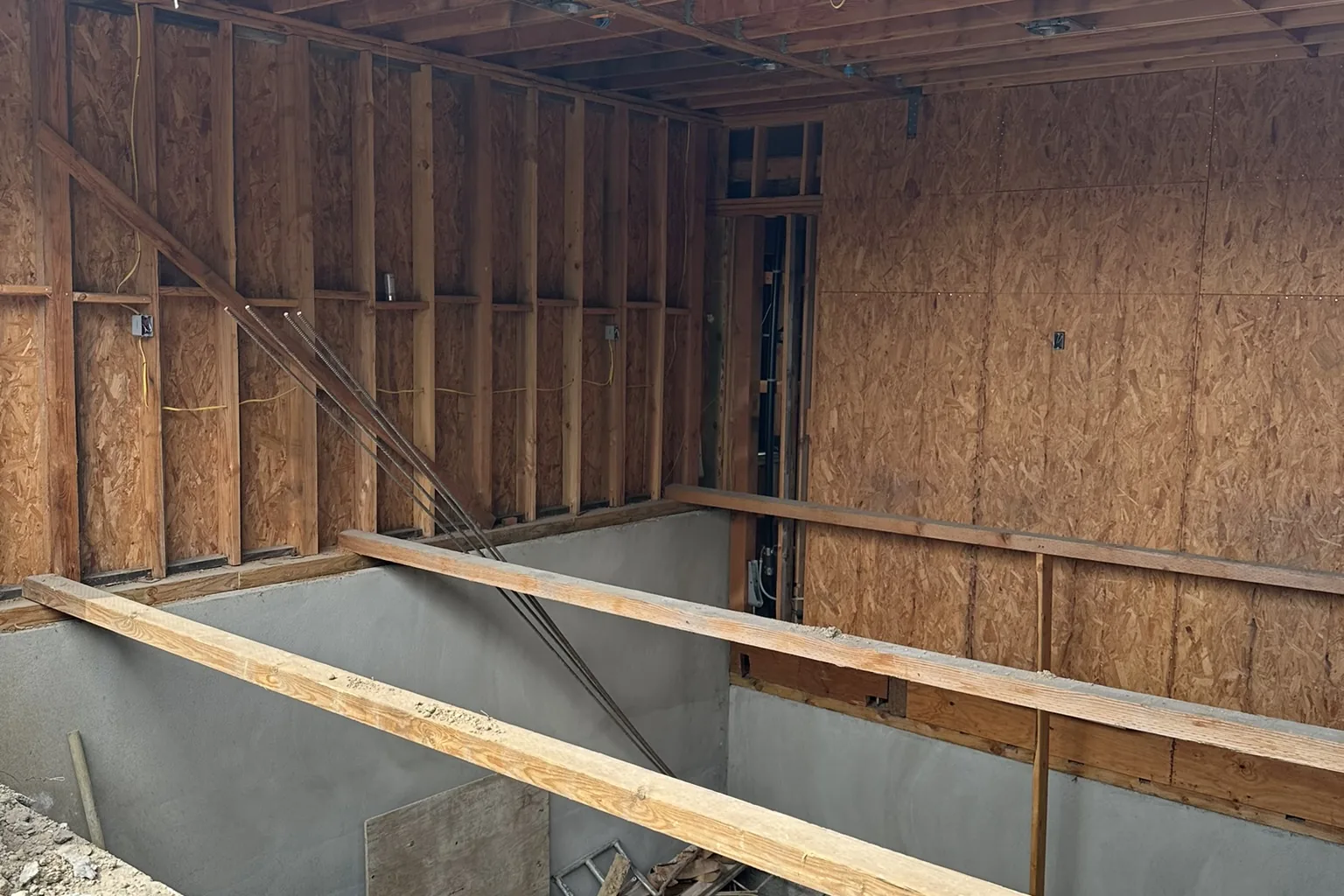 A below-grade concrete level dug into the slope beneath the wood framing of an Akopi Builders hillside home in Bel Air.