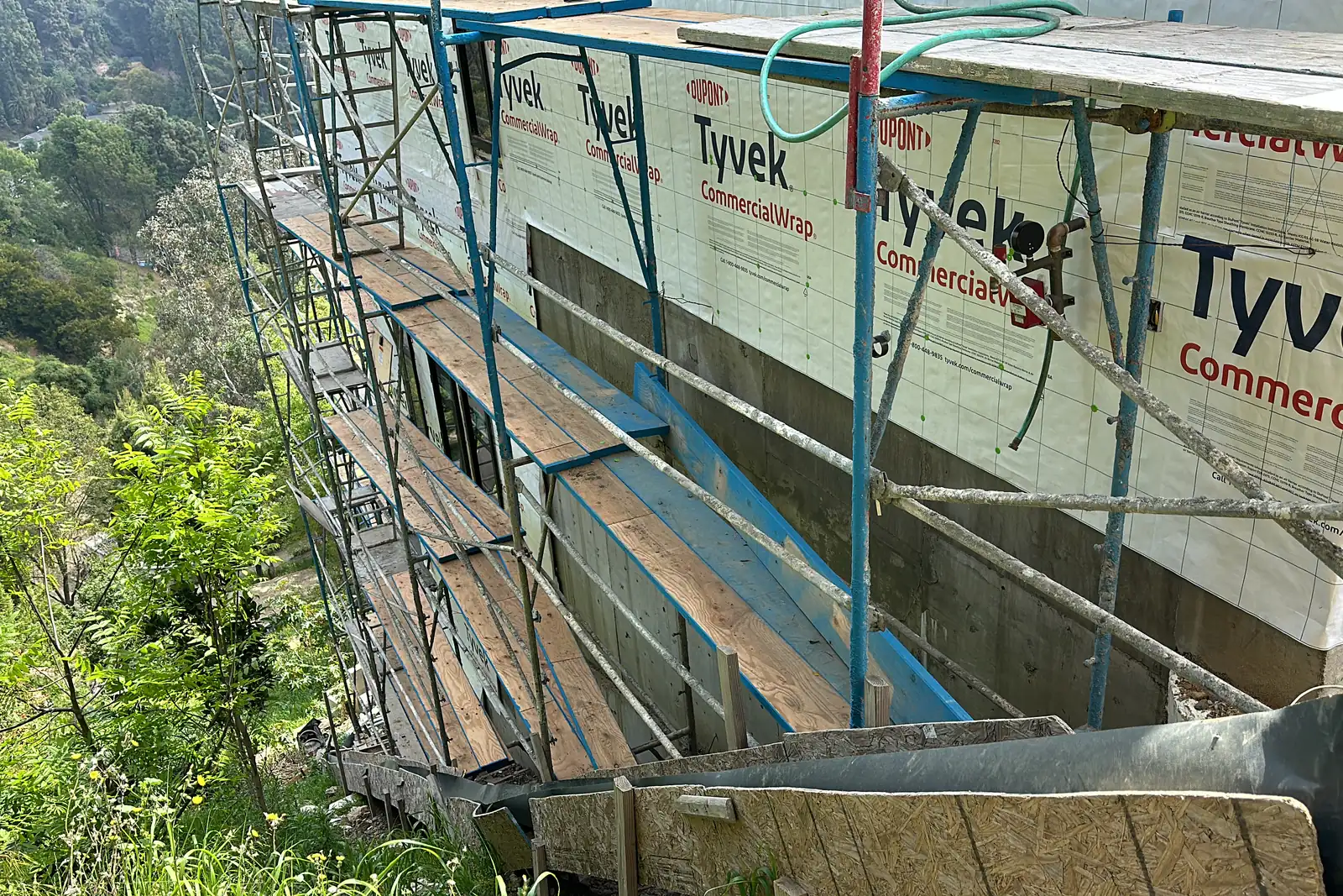Scaffolding along a wrapped wall of an Akopi Builders custom home under construction on a steep Bel Air hillside.