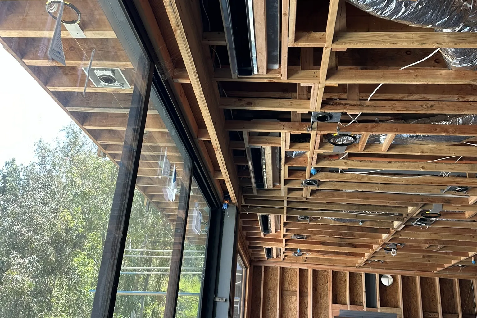 Open ceiling framing and a wall of glass looking out to trees, inside an Akopi Builders custom home under construction in Bel Air.
