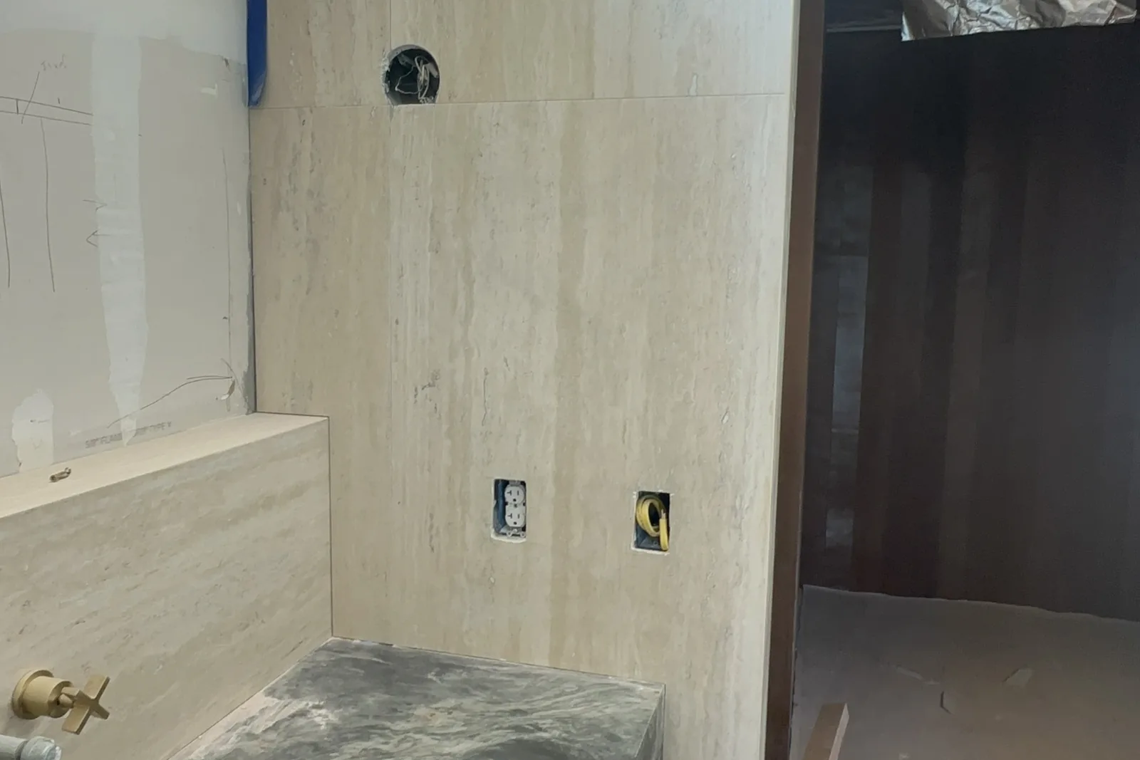 A green veined stone vanity and travertine walls in a primary bathroom under construction, in an Akopi Builders custom home in Bel Air.