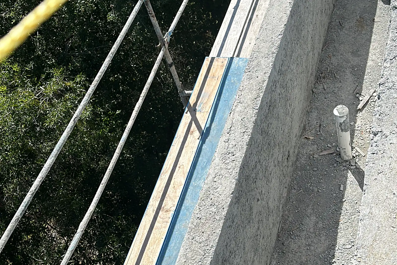 Looking down the top of a new poured concrete retaining wall on a steep hillside lot, with scaffolding and trees below, at an Akopi Builders custom home in Bel Air.