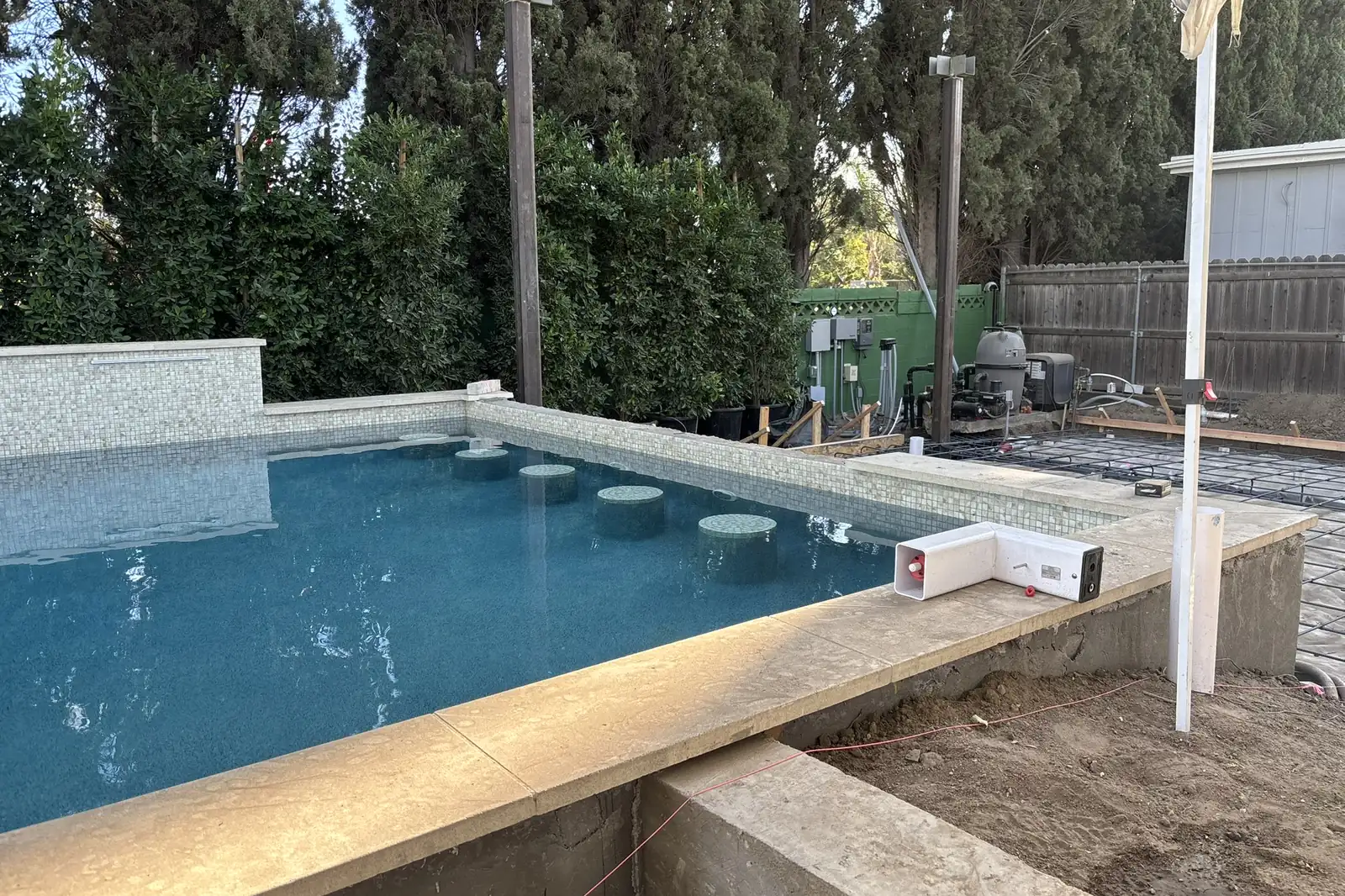 A newly filled pool with stone coping and a raised spa wall, deck work still in progress, at Arnwood, an Akopi Builders outdoor build in Los Angeles.