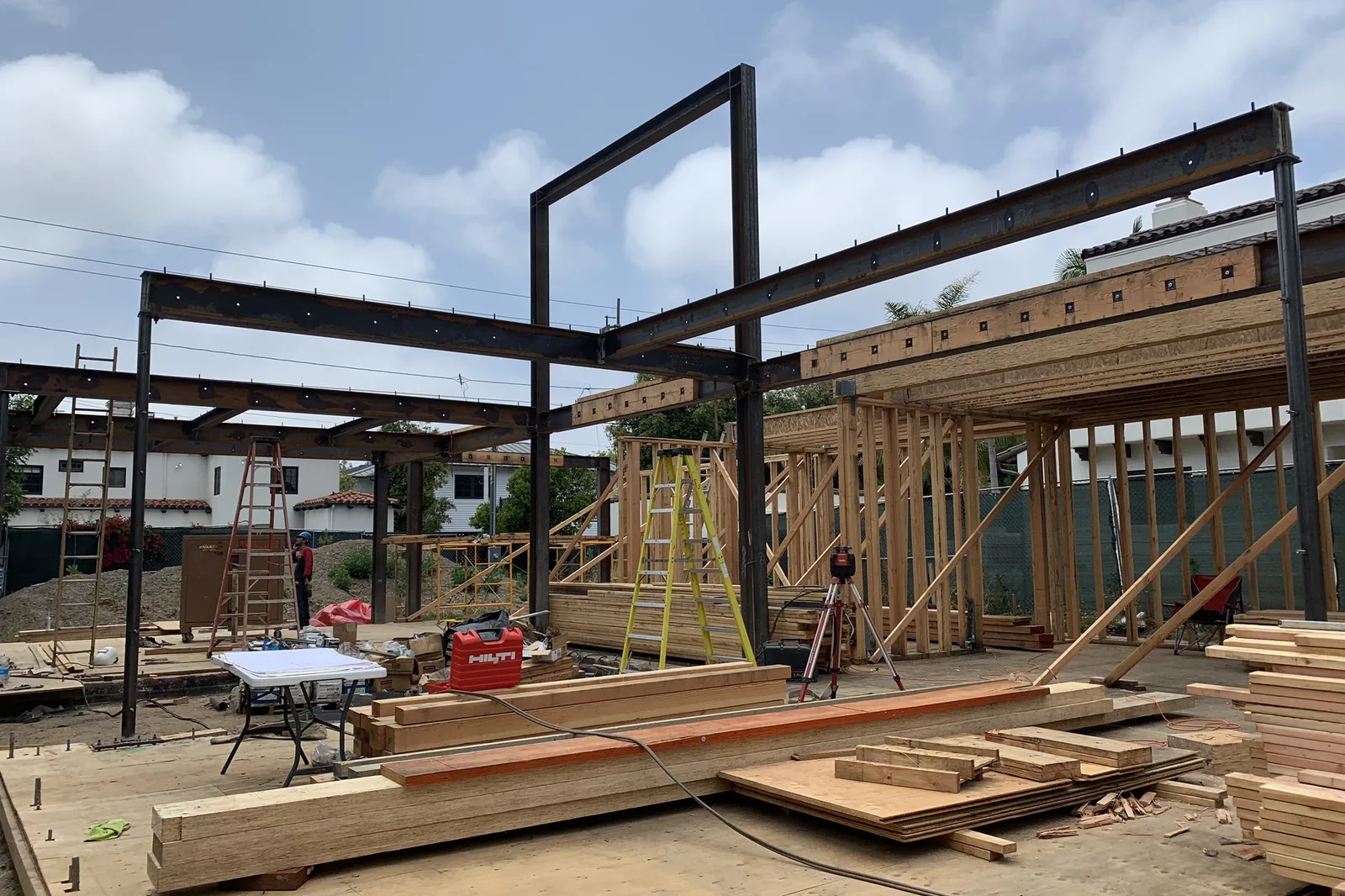 Steel beams and wood wall framing going up on a house under construction in Santa Monica, with lumber stacked on the floor deck, an Akopi Builders project.