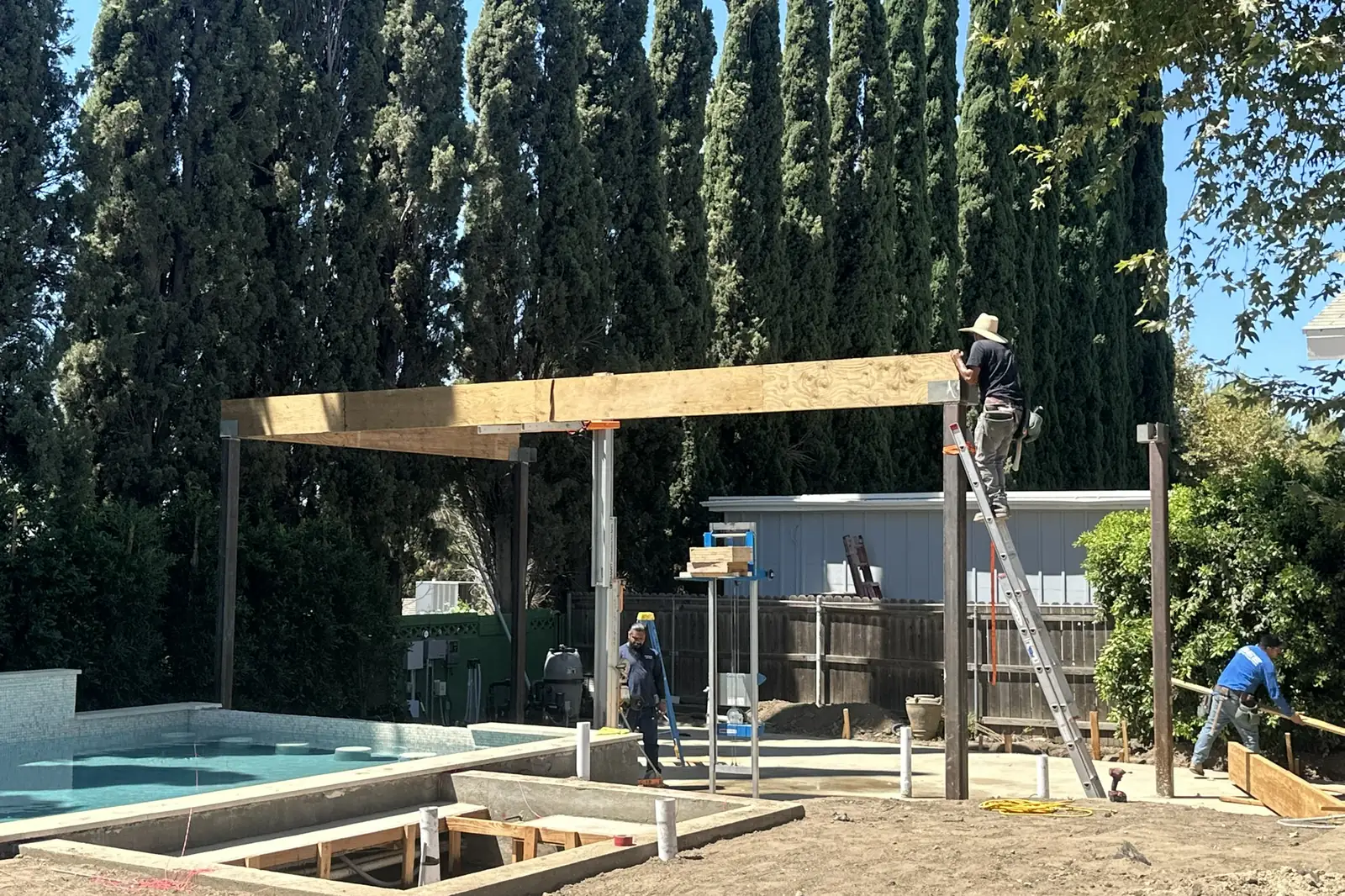Crew framing a wood pergola with posts and beams beside a new pool at Arnwood, an Akopi Builders outdoor build in Los Angeles.