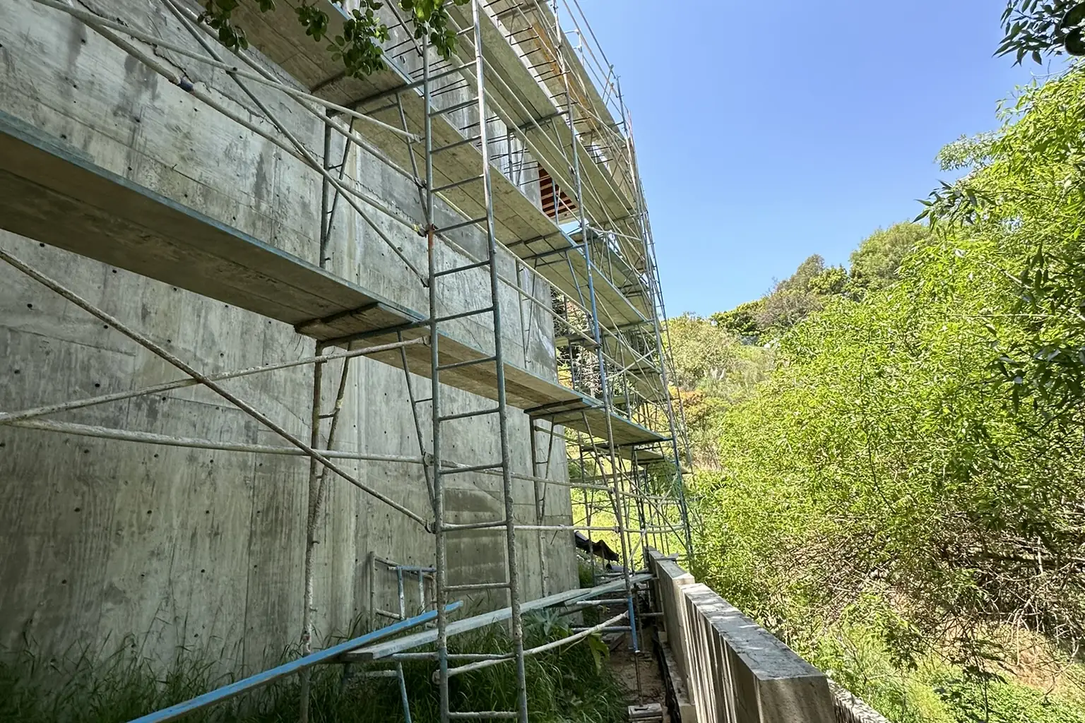 A concrete retaining wall under scaffolding on a hillside lot, at an Akopi Builders custom home build in Bel Air; it is not a Palisades rebuild.