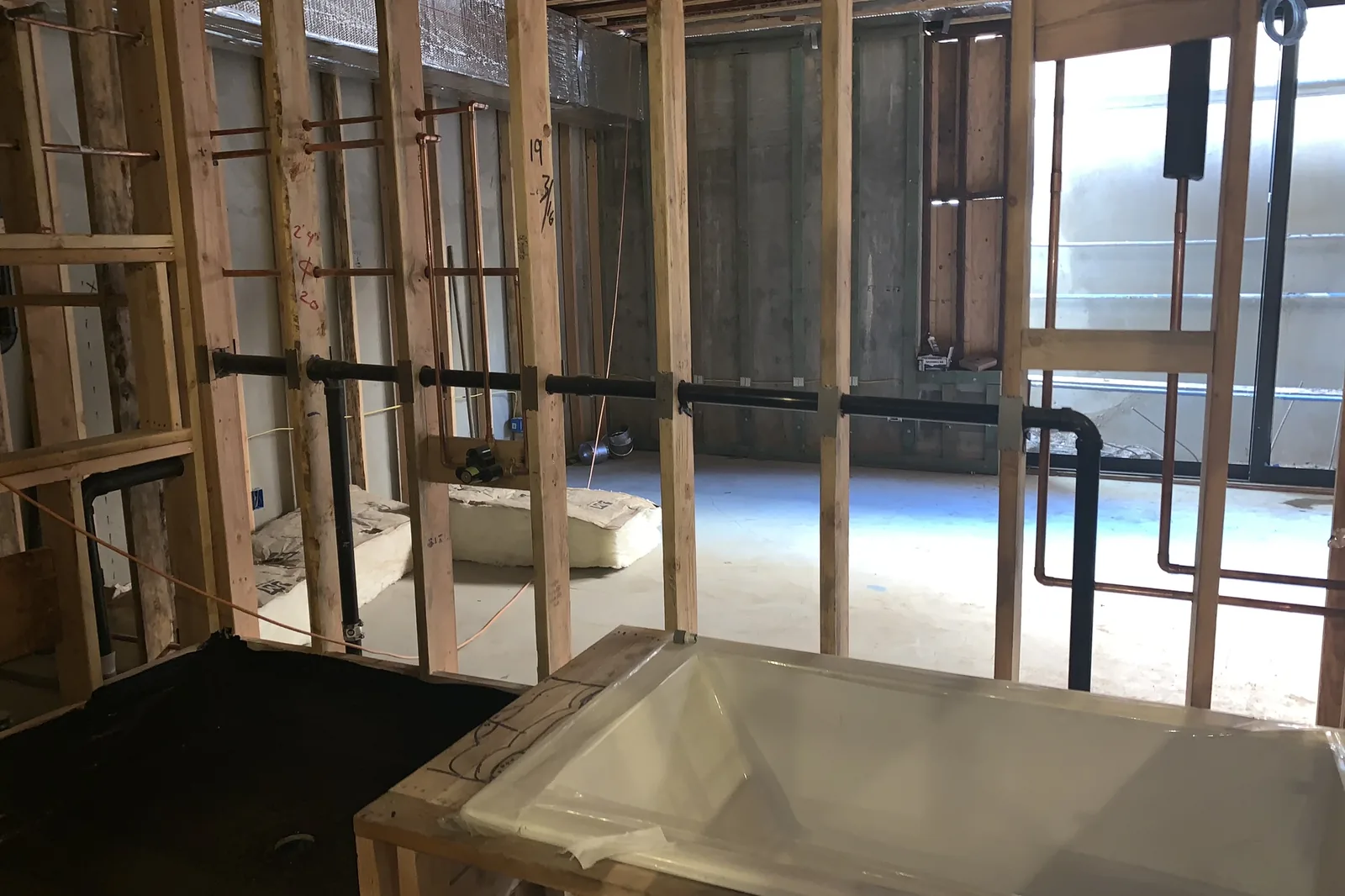 Open stud walls, new black drain pipes and copper supply lines, and a new tub set in its frame during an Akopi Builders bathroom remodel in Santa Monica.