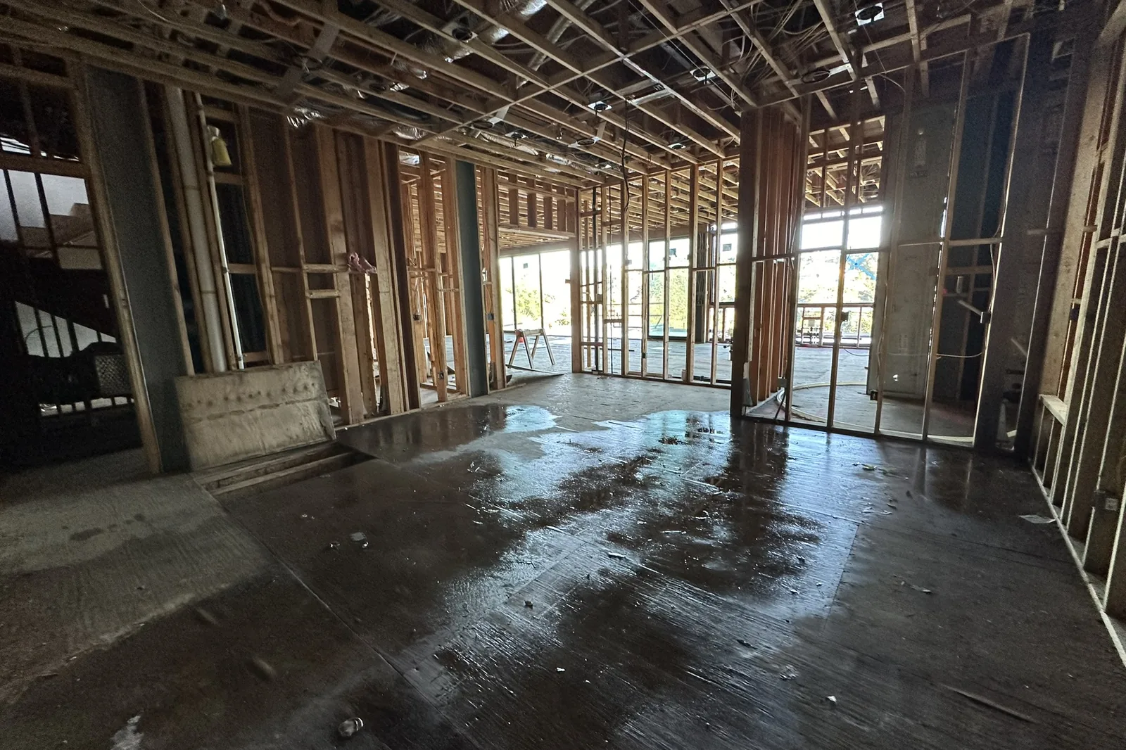A wide room opened to bare wood studs and ceiling joists, with tall window openings at the back, on an Akopi Builders project in Bel Air.
